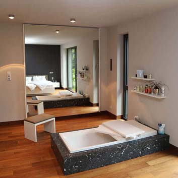 Contemporary bedroom with a wooden floor-embedded bathtub with Corian trim