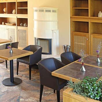 Café with wall-to-wall base cabinets featuring wooden frame fronts with rattan inserts and white knobs as pointers, open wooden shelves above and below the ceiling closed cabinets, square 2-person tables on one leg and chairs next to the tables.