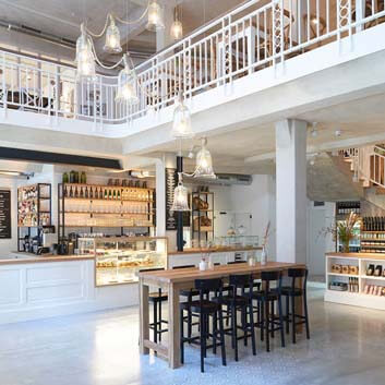 Restaurant in Hamburg, white interiors, with open loft and staircase, large white counter serving as a bar seating area as well, with displayed food.