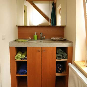 Badezimmer mit hohem Waschtischunterschrank mit fugenloser Waschtischplatte aus Corian in warmem Holz mit 2 Türen und offenem Regal