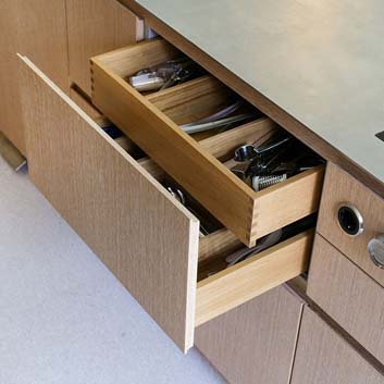 Nahaufnahme einer offenen Schublade aus Holz mit Besteck und Innenschublade mit sichtbarer Holzverbindung, sichtbare Bora-Bedienelemente