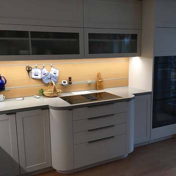 Moderne graue Küche mit einem geschwungenen, nach vorne gerichteten Schrank mit Bora-Induktionsherd, grauer nahtloser Arbeitsplatte, einem eingebauten Weinkühlschrank, einer funktionalen Rückwand mit 2 Schienen zum Aufhängen kleiner Küchenutensilien und 2 kleinen Glasregalen