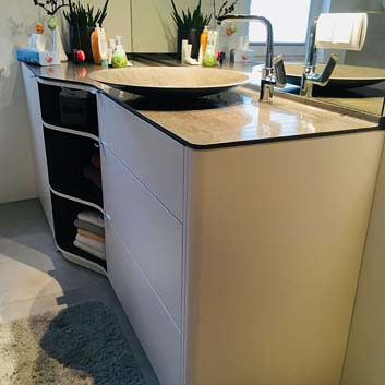 A sleek and elegant curved vanity cabinet with a thin surface, a flat bowl-like sink, featuring 3 drawers, doors, and open shelves