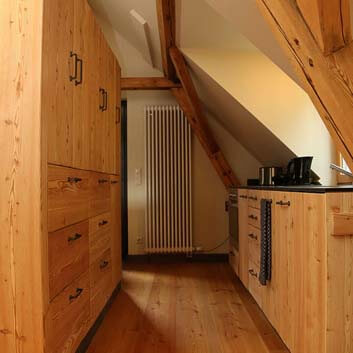 Natural wood kitchen with visible wood texture, alpine hut feeling with chunky black U-handles, wooden floor, and sloping wooden beams