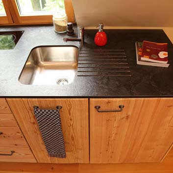 Close-up of natural wood kitchen with black textured grooved Corian surface and seamless induction hob on the back of the countertop