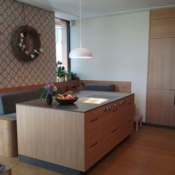 Wooden kitchen island with built-in Bora stove and extractor in a Corian countertop, L-shaped wooden bench with padded gray cushions.