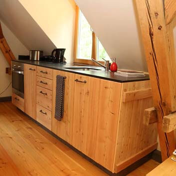 Kitchen made of natural wood with visible wood texture, Corian Black textured countertop, recessed sink, and oven