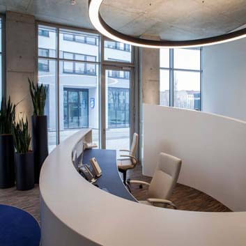 Curved, open elliptical counter made of white Corian with a round LED ceiling light above it.