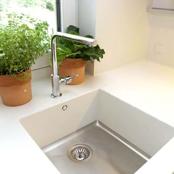 Corian-Arbeitsplatte mit einer nahtlosen Mixa Corian-Spüle mit Metallboden und weißen Seiten, silberner hoher Küchenwasserarmatur und 2 Töpfen mit Kräutern