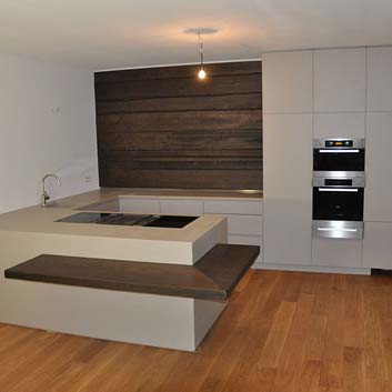 U-förmige graue Küche mit einer Holzwand aus dunklem Holz, mit grauer Arbeitsplatte und professionellem Bora-Herd mit Dunstabzug und Miele-Backofen