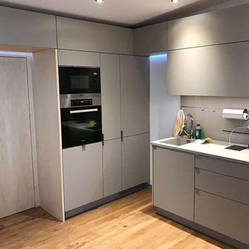 Graue, minimalistische Küche mit verdecktem Kühlschrank, eingebauter Miele-Mikrowelle und Backofen Corian-Arbeitsplatte mit nahtloser Küchenspüle, funktionaler Spritzschutz mit Schiene, magnetischer Messerblock